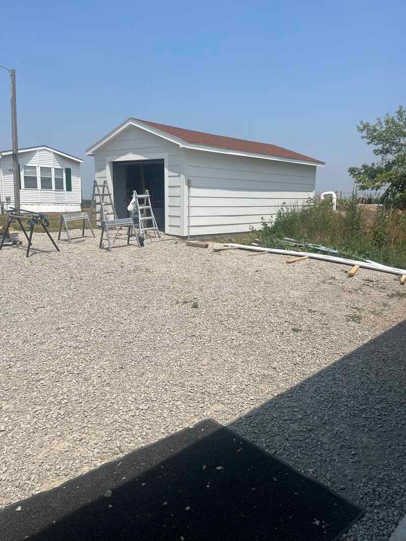 A white shed with a red roof is sitting on top of a gravel lot.
