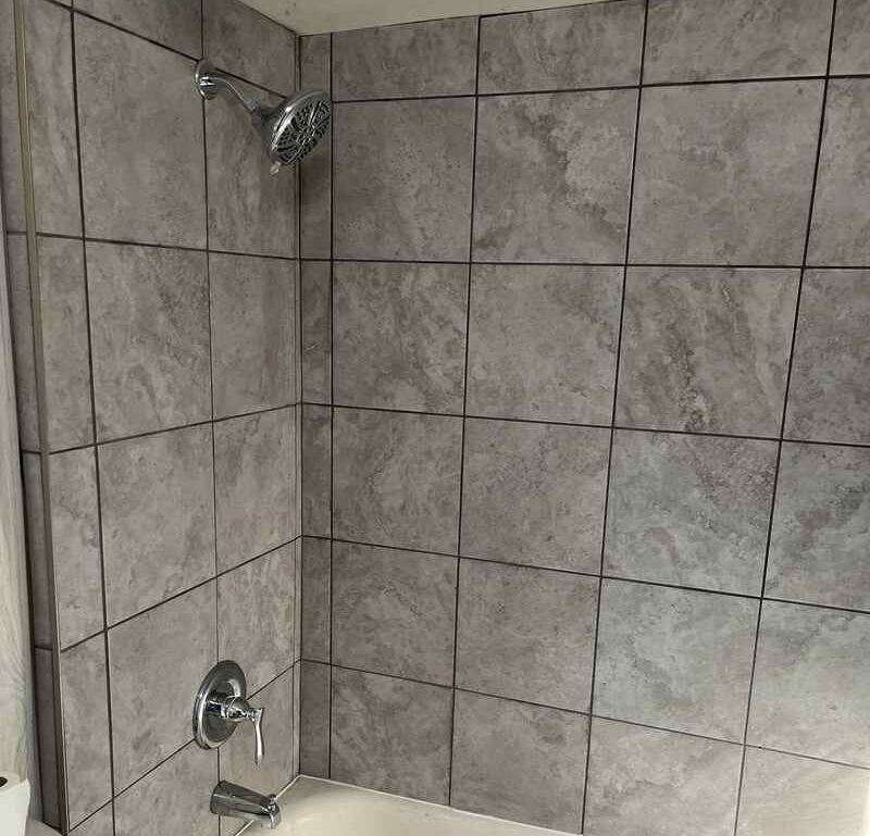 A bathroom with gray tiles and a shower head.