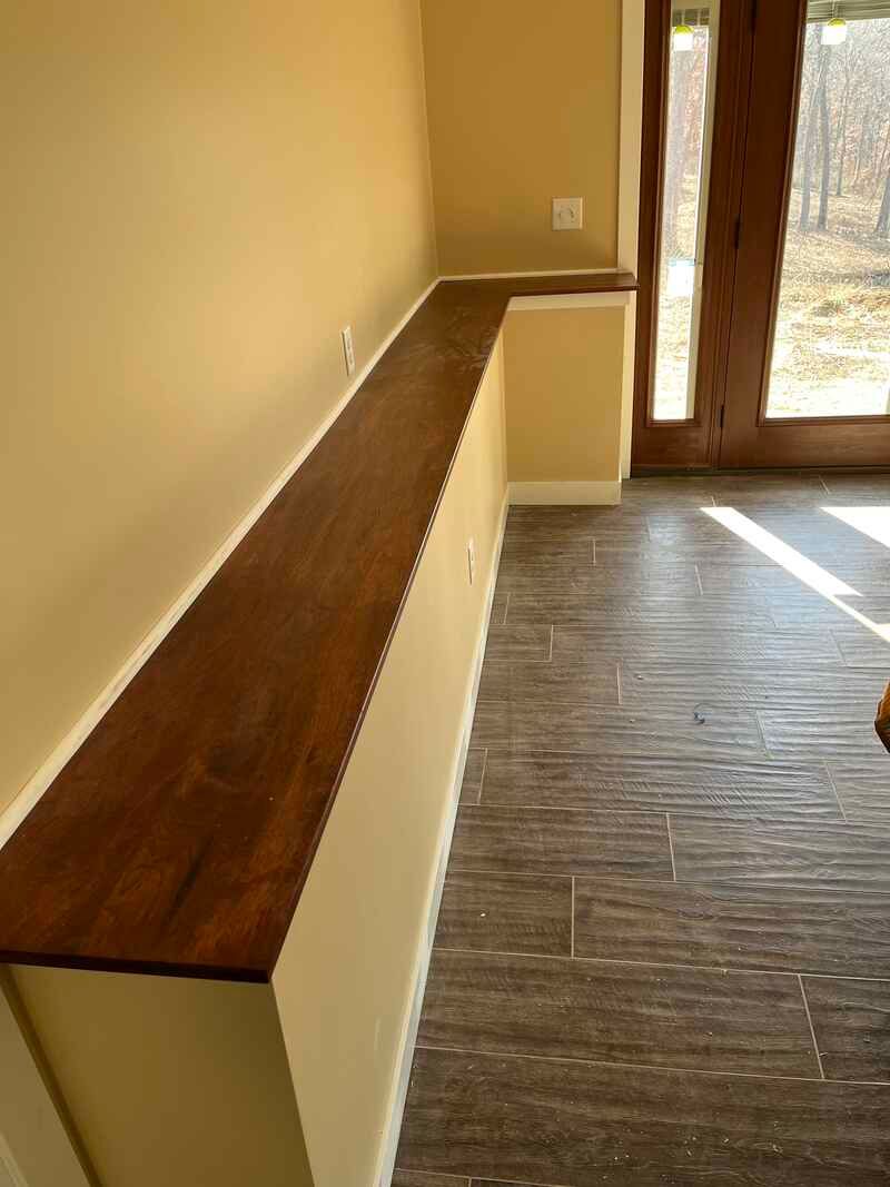 A long wooden bench in a room next to a window.