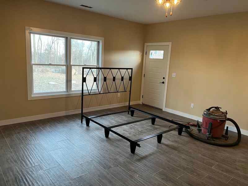 An empty room with a bed frame and a vacuum cleaner.