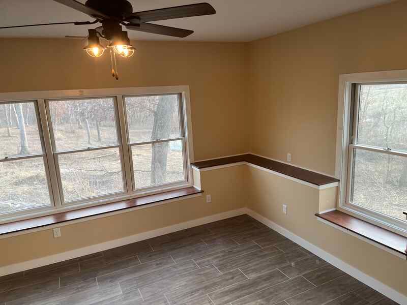 An empty room with a ceiling fan and two windows.