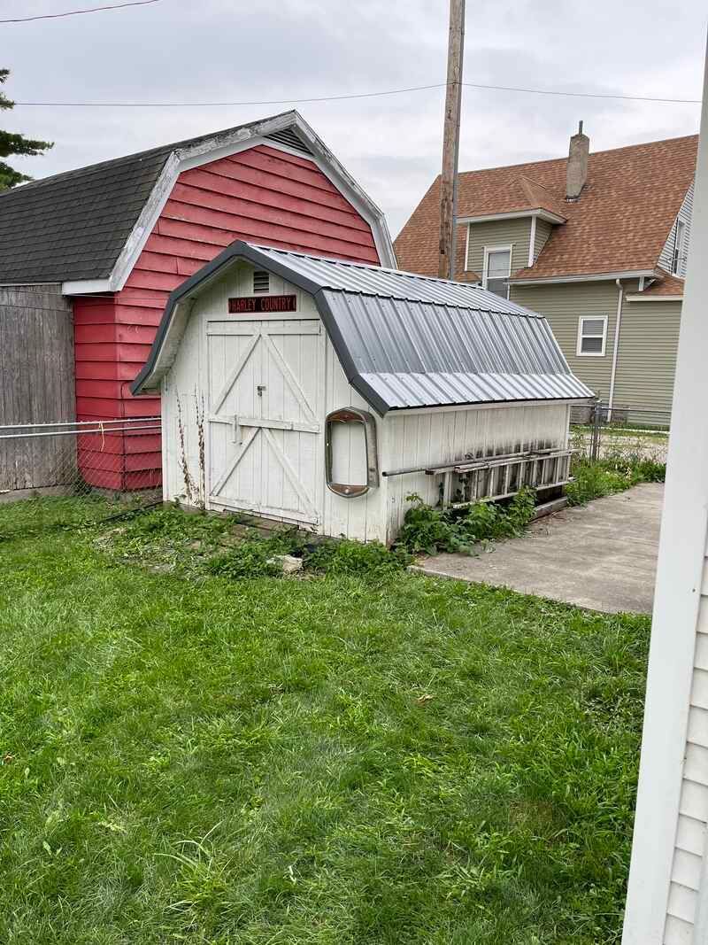 A white barn with a red roof is in the backyard of a house.