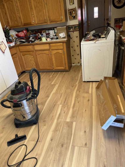 A vacuum cleaner is sitting on a wooden floor in a kitchen.
