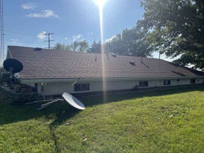 A large white house with a brown roof is sitting on top of a lush green field.