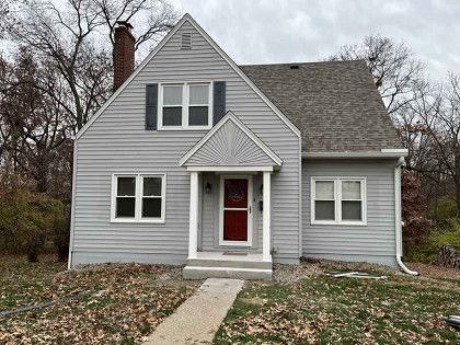A small gray house with a red door and a walkway in front of it.