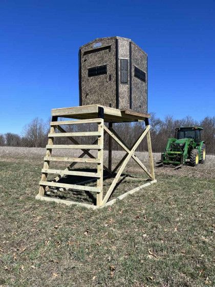 A deer blind is sitting in the middle of a field next to a tractor.