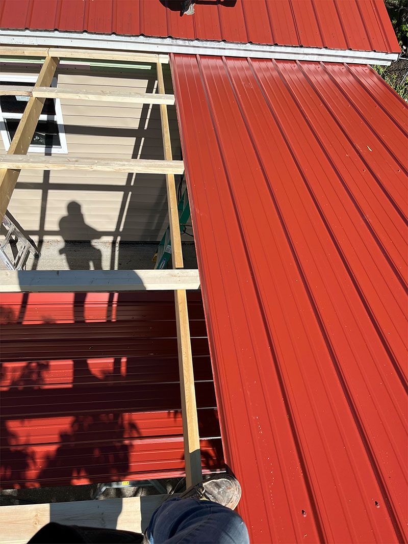 A person is standing on top of a red metal roof.