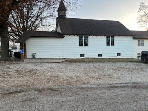 A white church with a brown roof is sitting in a gravel lot.