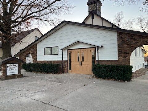 A church with a clock tower on top of it is sitting on the side of the road.