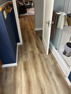 A hallway with hardwood floors leading to a bathroom.