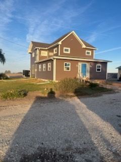 A blue house with a brown roof is sitting on top of a dirt field.