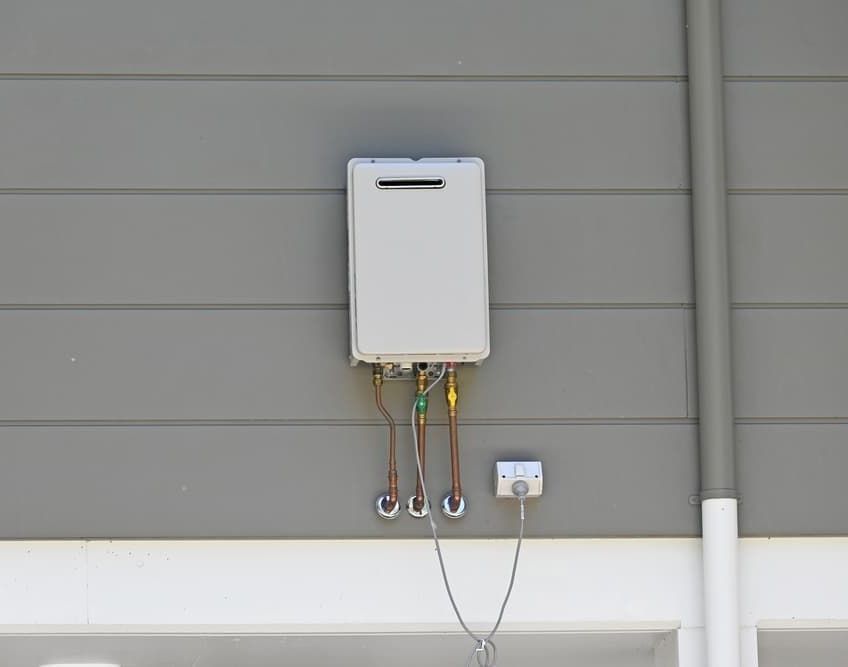 A White Water Heater is Attached to the Side of a House — SOS Hot Water & Plumbing Services in Gerringong, NSW