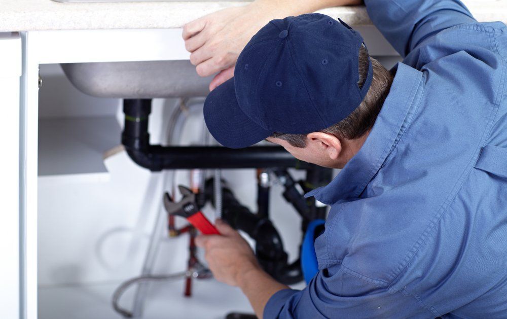 Plumber in blue uniform repairing pipes under a kitchen sink using a wrench
