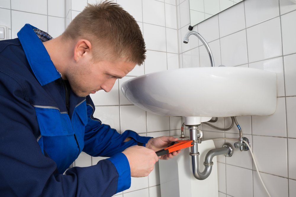 A Plumber is Fixing a Sink in a Bathroom With a Wrench — SOS Hot Water & Plumbing Services in Gerringong, NSW