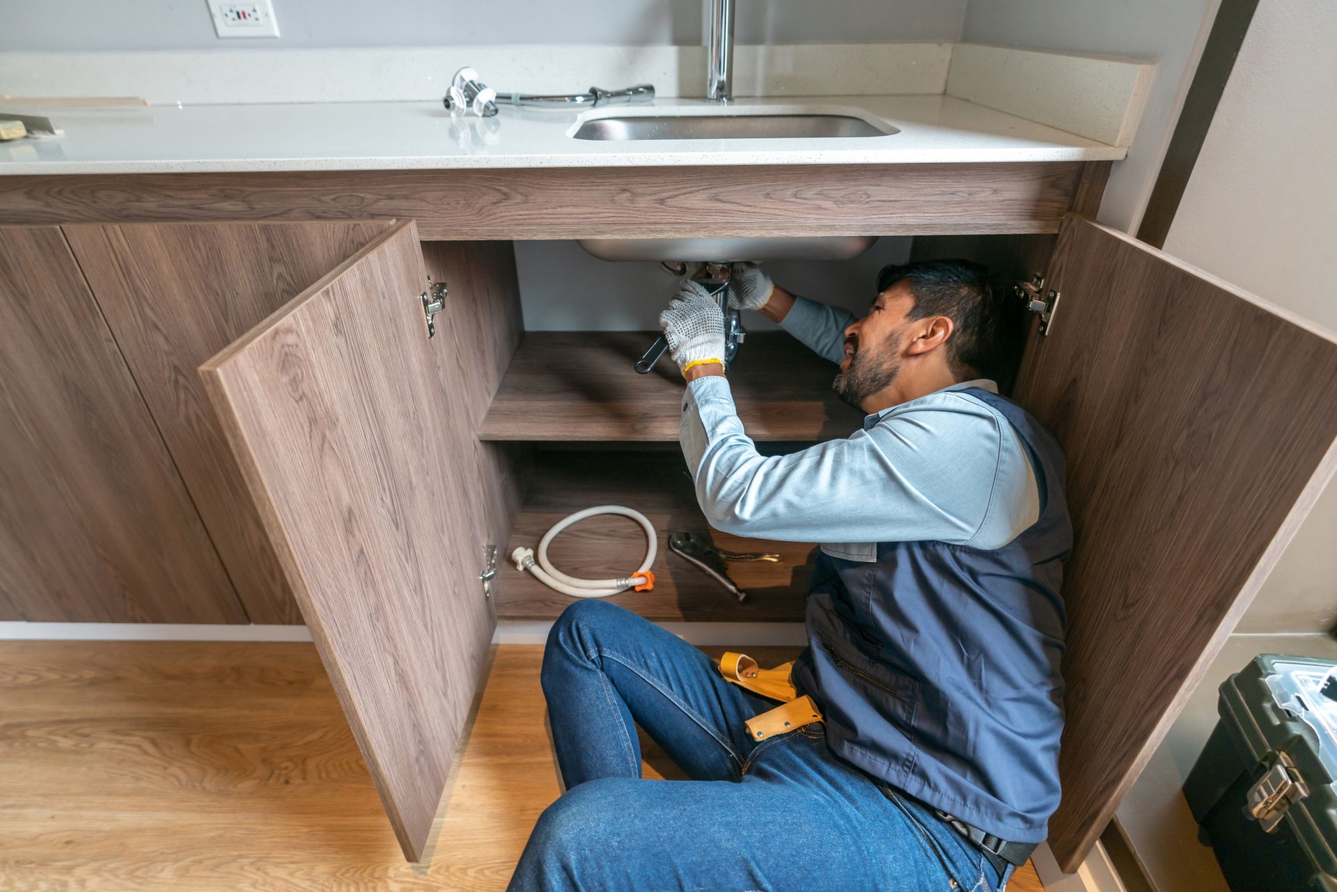 A plumber fixing a leak in the kitchen sink of a house.