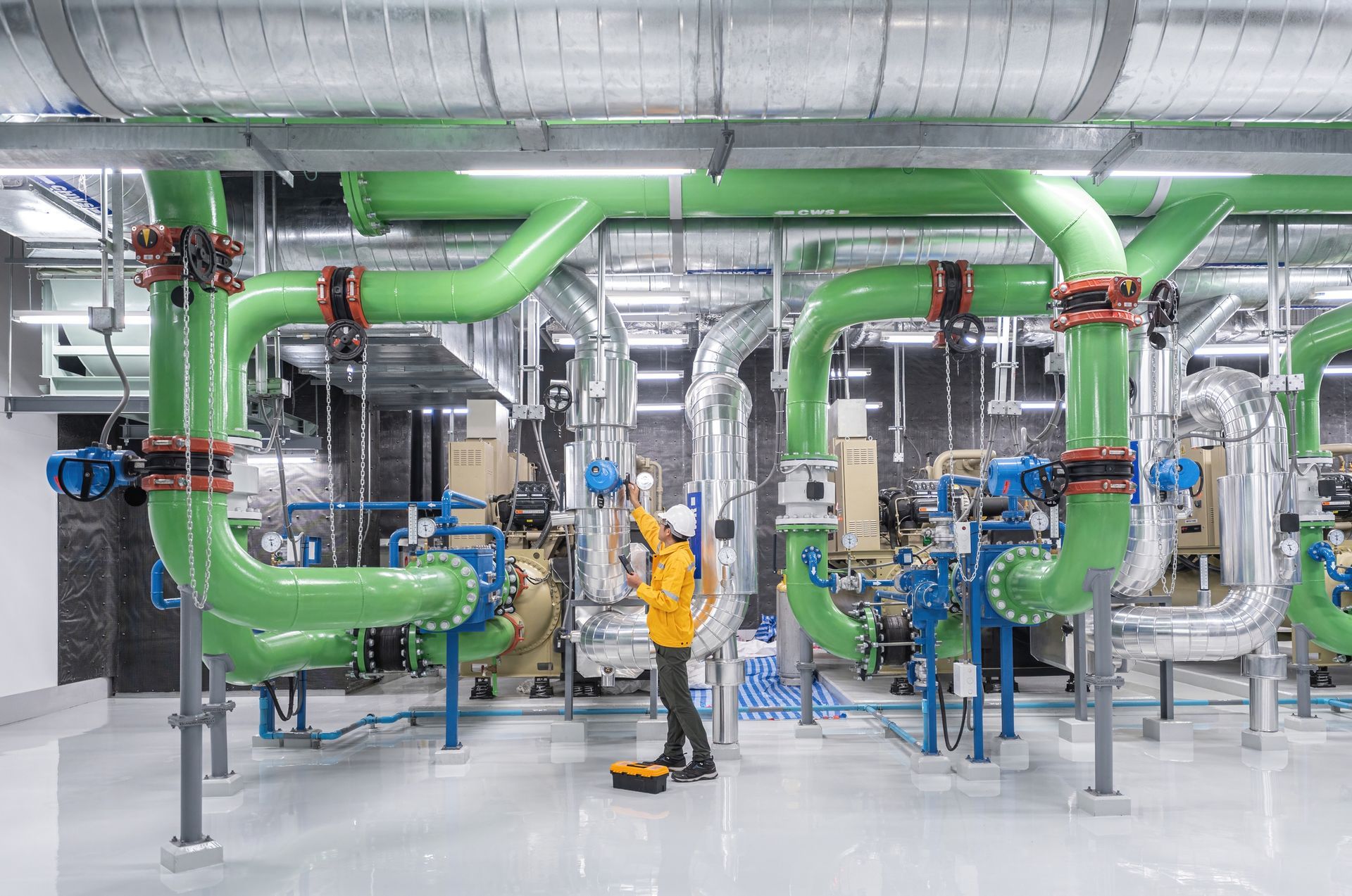 Technician inspecting green pipes and valves during industrial plumbing service maintenance. 