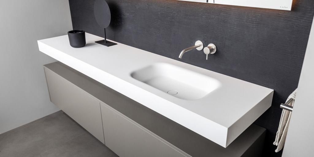 Moderne badkamermeubel met een wit aanrechtblad en ingebouwde wastafel, grijze kast en zwarte structuurmuur.