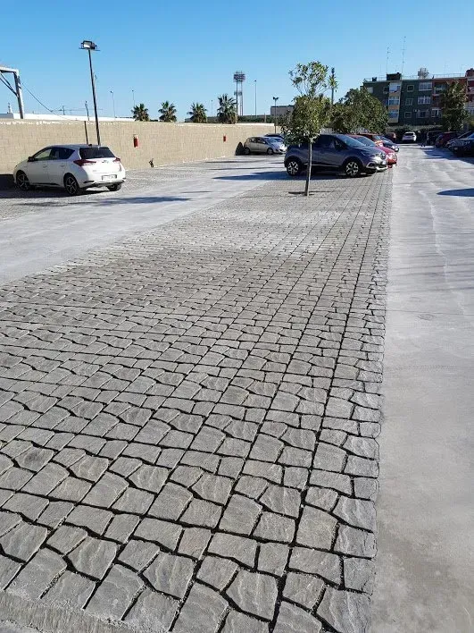 Parcheggio lastricato in pietra con auto parcheggiate e un muro sullo sfondo.