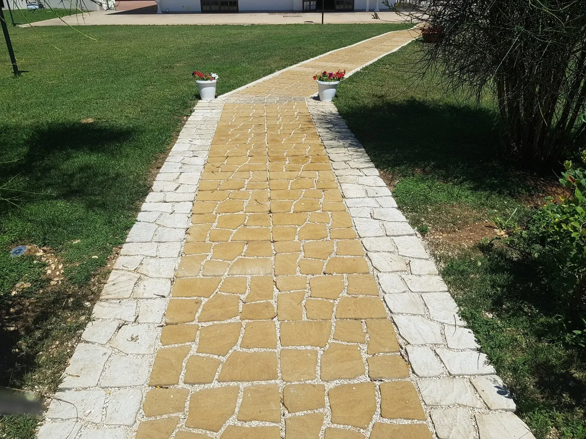 Un sentiero acciottolato fiancheggiato da vasi di fiori conduce attraverso un prato verde verso un edificio.