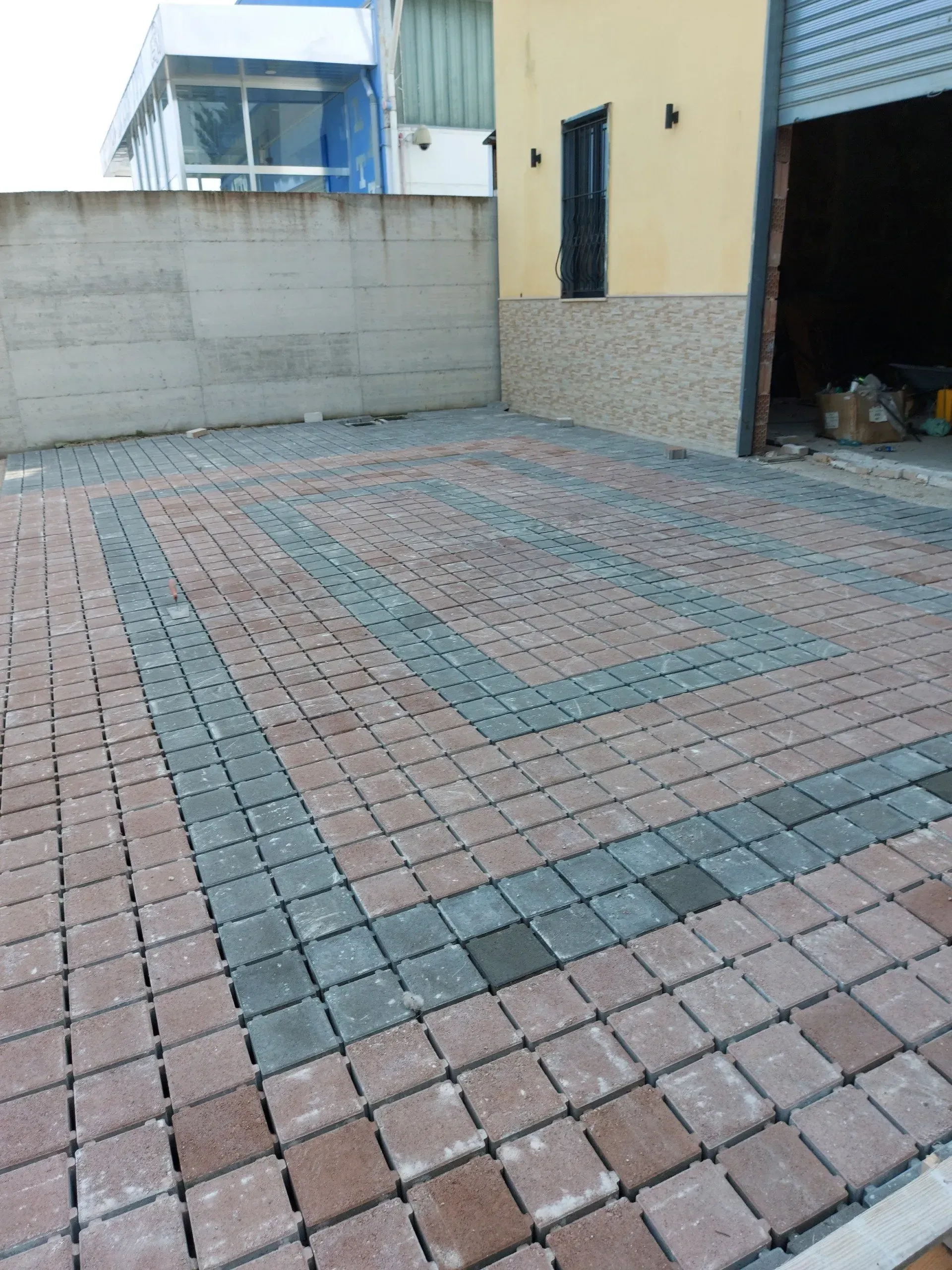 Vialetto in mattoni con blocchi rossi e grigi, accanto a un edificio con un portone del garage chiuso.