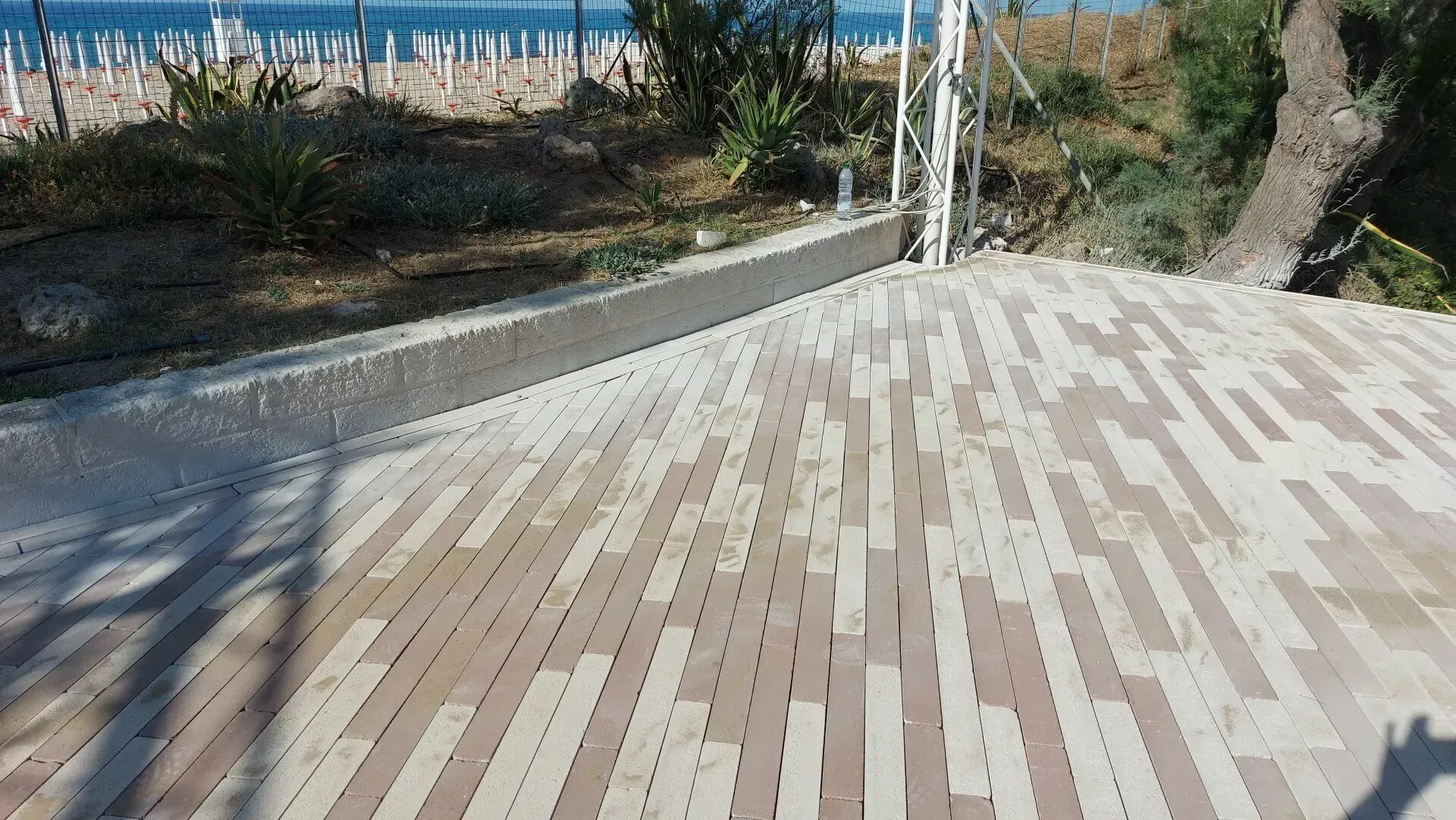 Patio piastrellato con spiaggia sullo sfondo. Motivo a mattoni marrone chiaro e scuro.