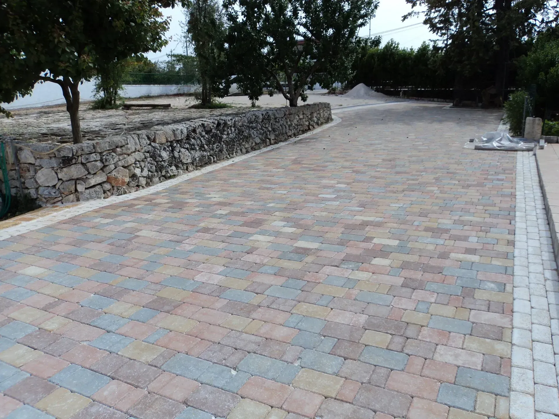 Vialetto pavimentato in mattoni, delimitato da un muro in pietra e da alberi.