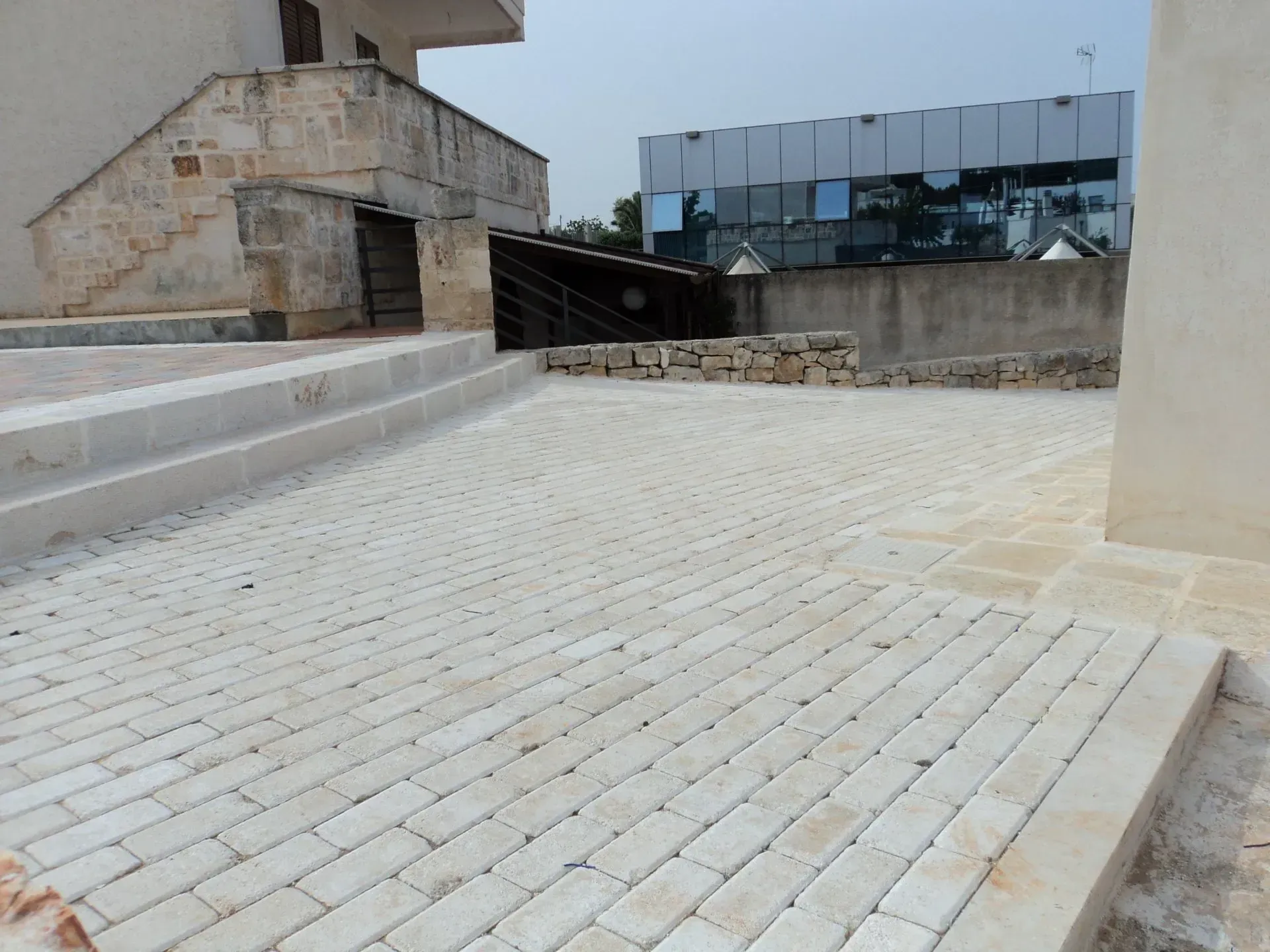 Spazio esterno pavimentato in mattoni con gradini, edifici sullo sfondo.