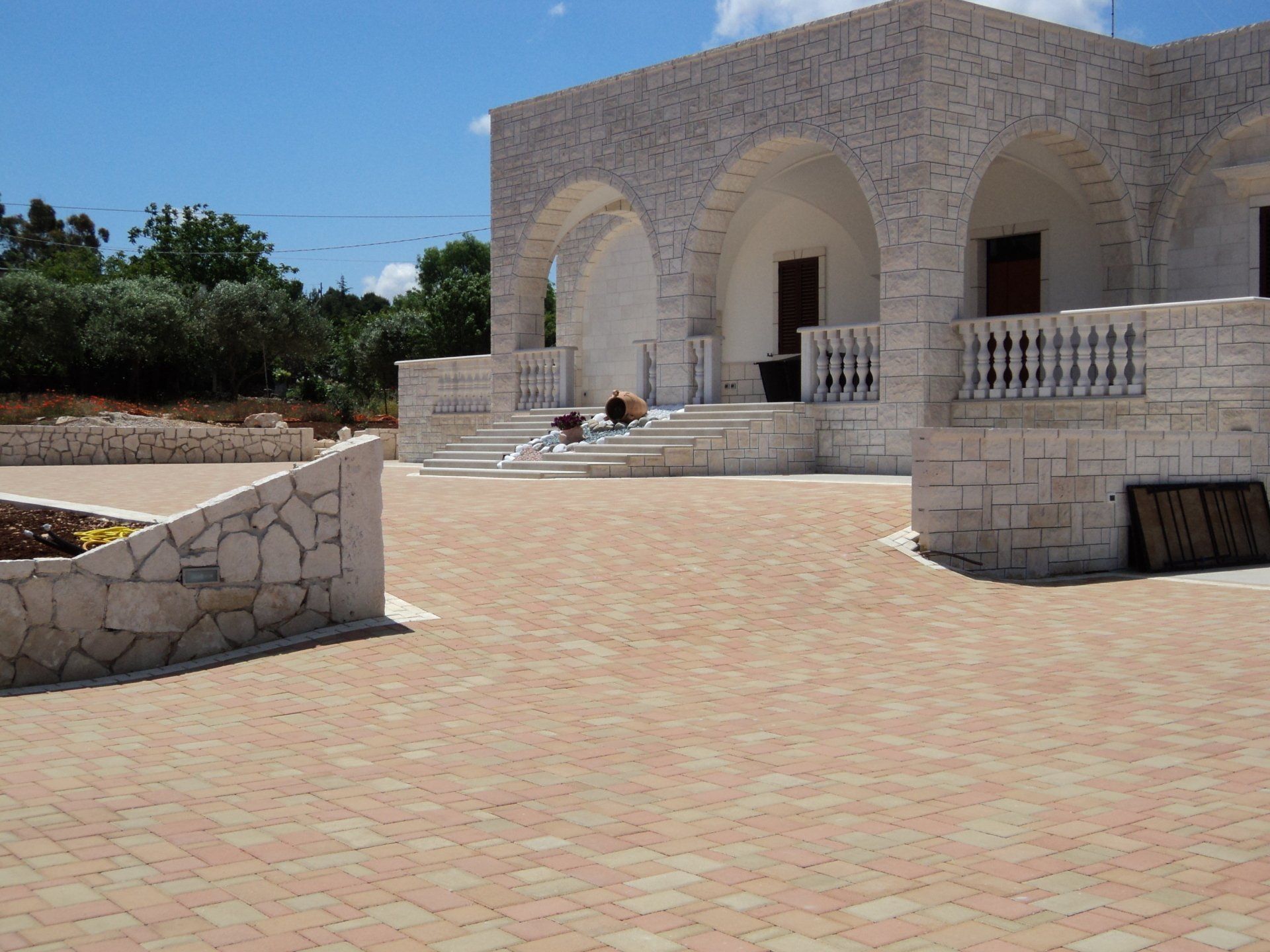 Edificio in pietra con ingressi ad arco e un patio pavimentato in mattoni sotto un cielo azzurro brillante.