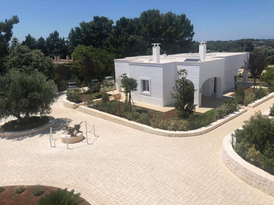 Casa in stucco bianco con giardino paesaggistico e vialetto pavimentato sotto un cielo azzurro.