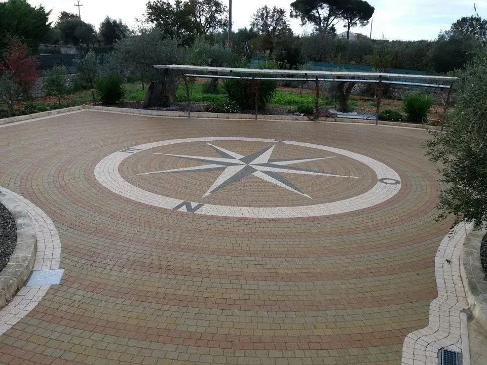 Vialetto in mattoni con al centro una rosa dei venti e alberi sullo sfondo.