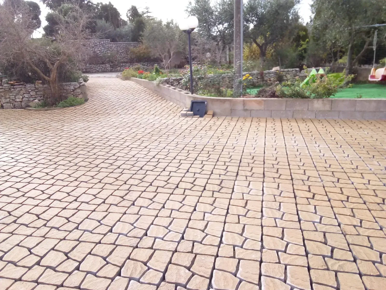 Vialetto di ciottoli gialli che conduce a un giardino con alberi e un parco giochi.