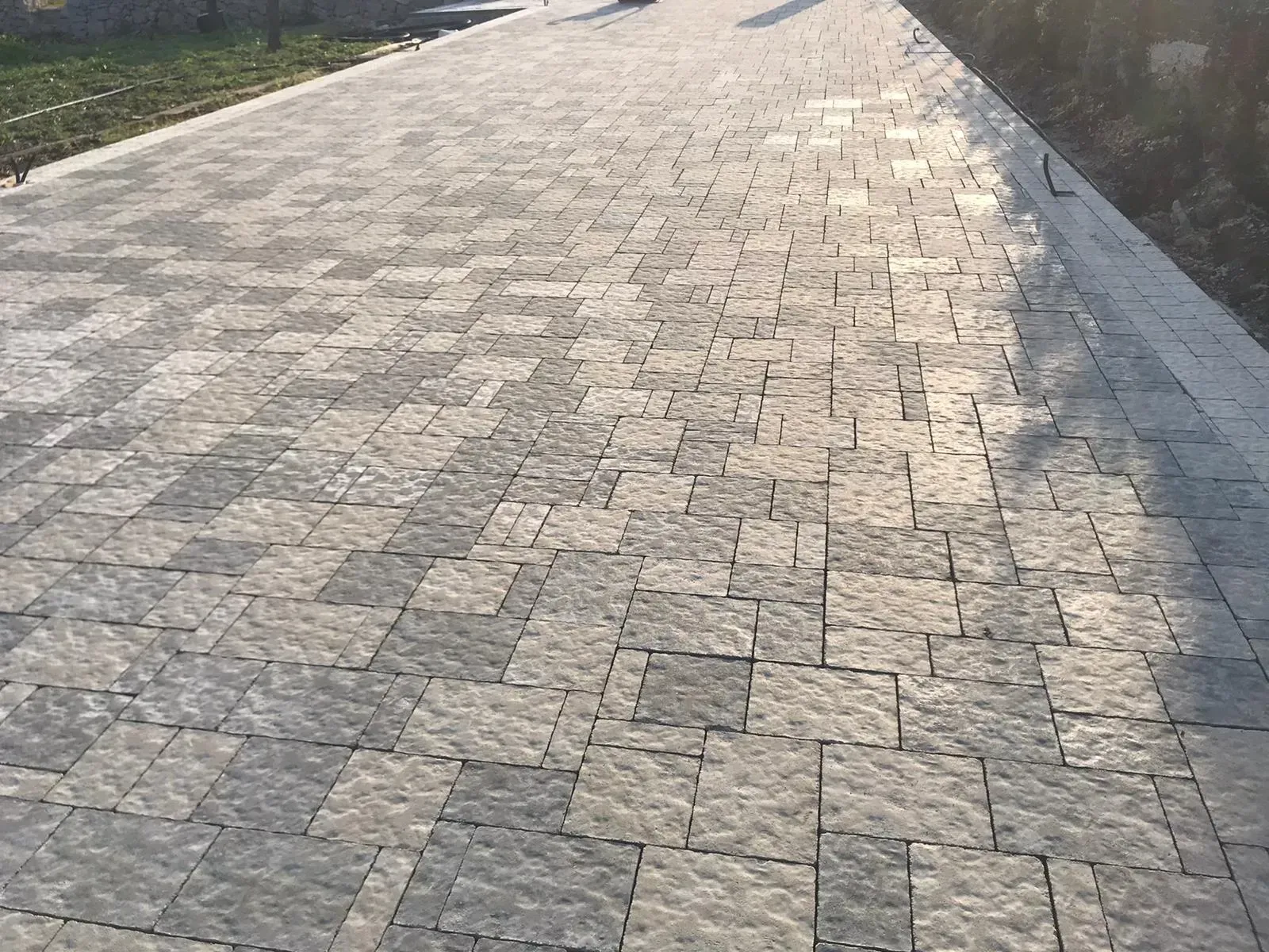 Percorso lastricato con pietre squadrate grigie e chiare. La luce del sole crea ombre.