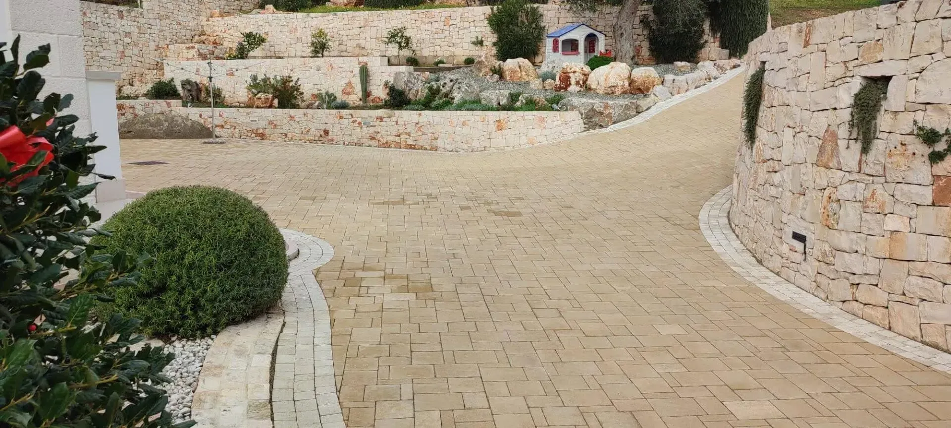 Un sentiero in pietra si snoda attraverso un cortile paesaggistico con muri terrazzati e un cespuglio arrotondato.