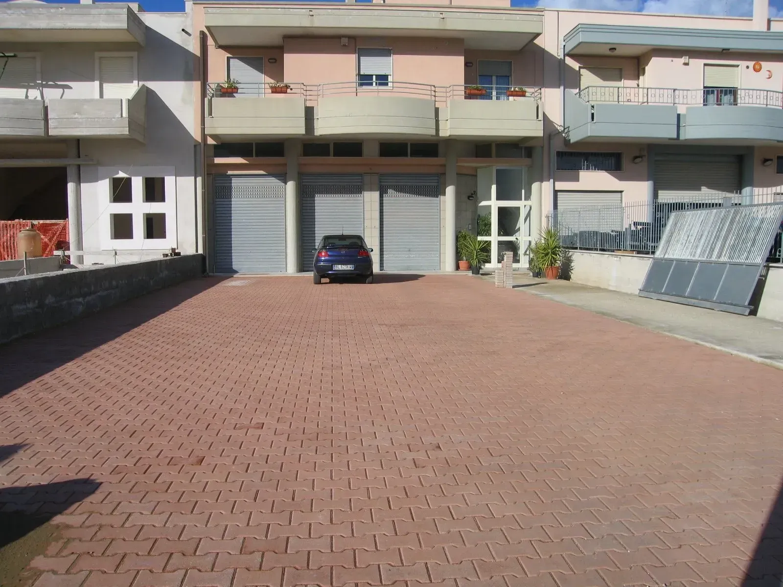 Parcheggio pavimentato in mattoni di fronte alle villette a schiera. Un'auto è parcheggiata vicino ai portoni dei garage chiusi.