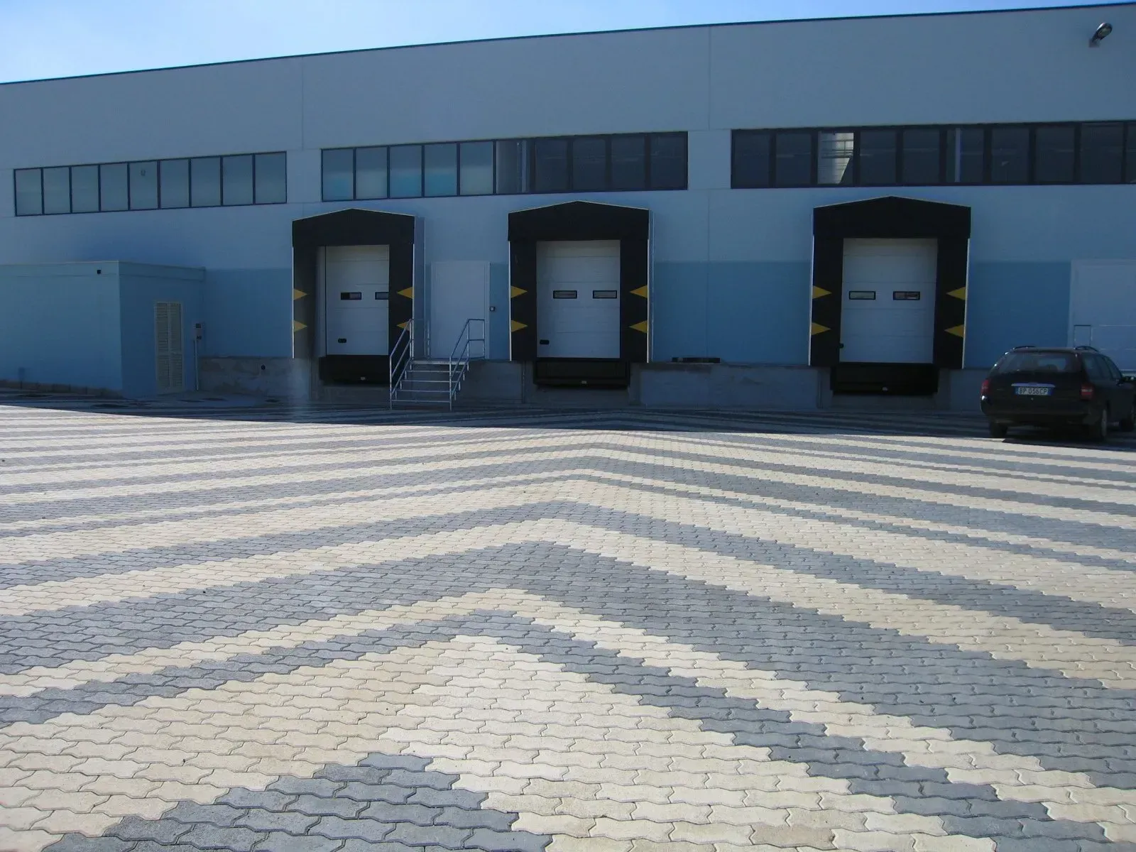 Magazzino con tre banchine di carico; lotto pavimentato in mattoni a spina di pesce.