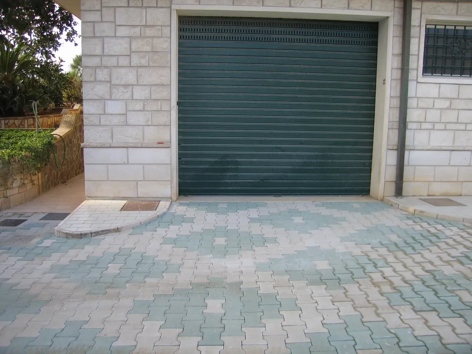 Portone di garage verde in un edificio in mattoni grigi, con pavimentazione decorata davanti.