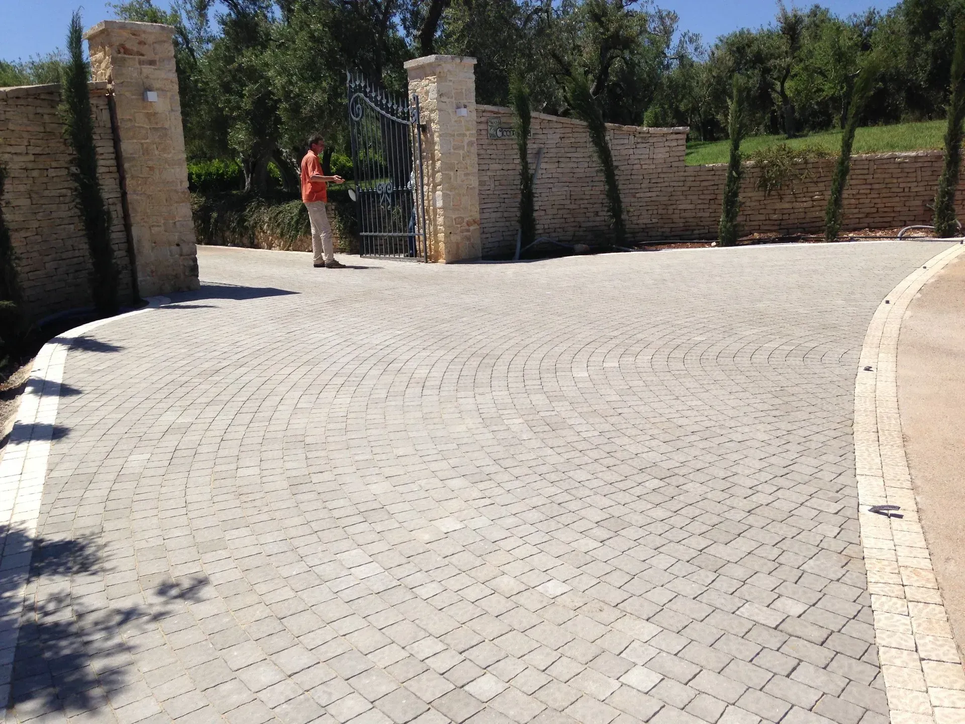 Vialetto in mattoni che conduce all'ingresso con cancello; un uomo è in piedi vicino al cancello in una giornata di sole.