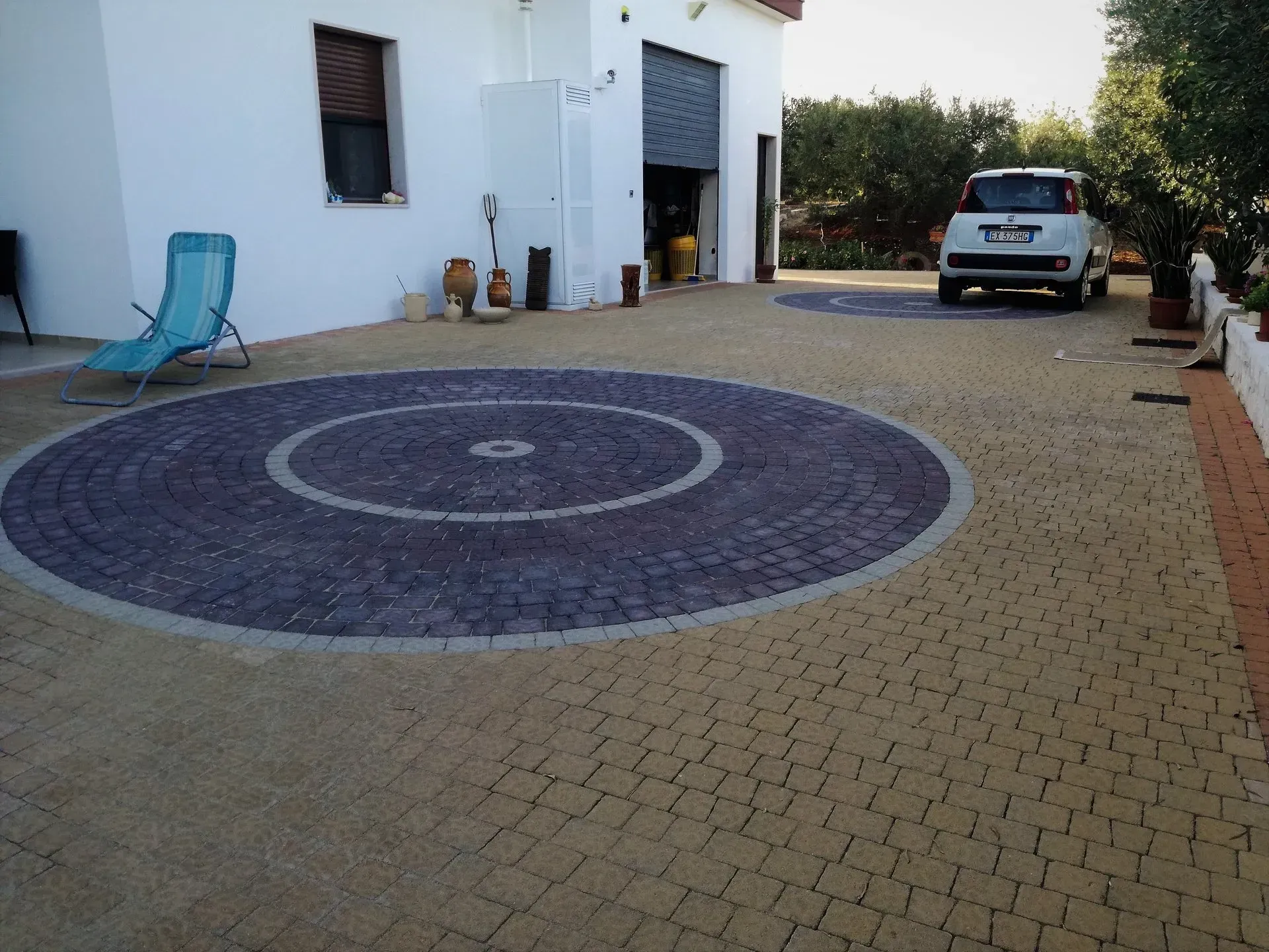 Vialetto d'accesso con pavimentazione circolare. Edificio bianco, auto e sedia in vista.