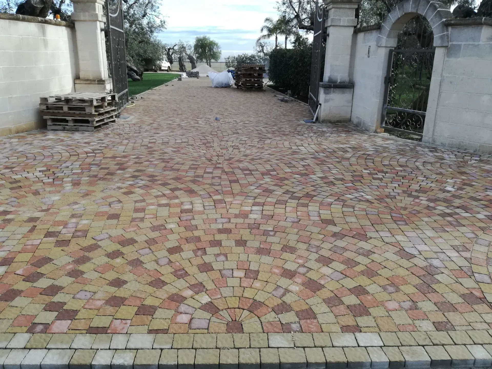 Vialetto d'accesso lastricato in mattoni con cancelli d'ingresso ad arco e muro, che conduce a una vista in lontananza sull'acqua e sul cielo.