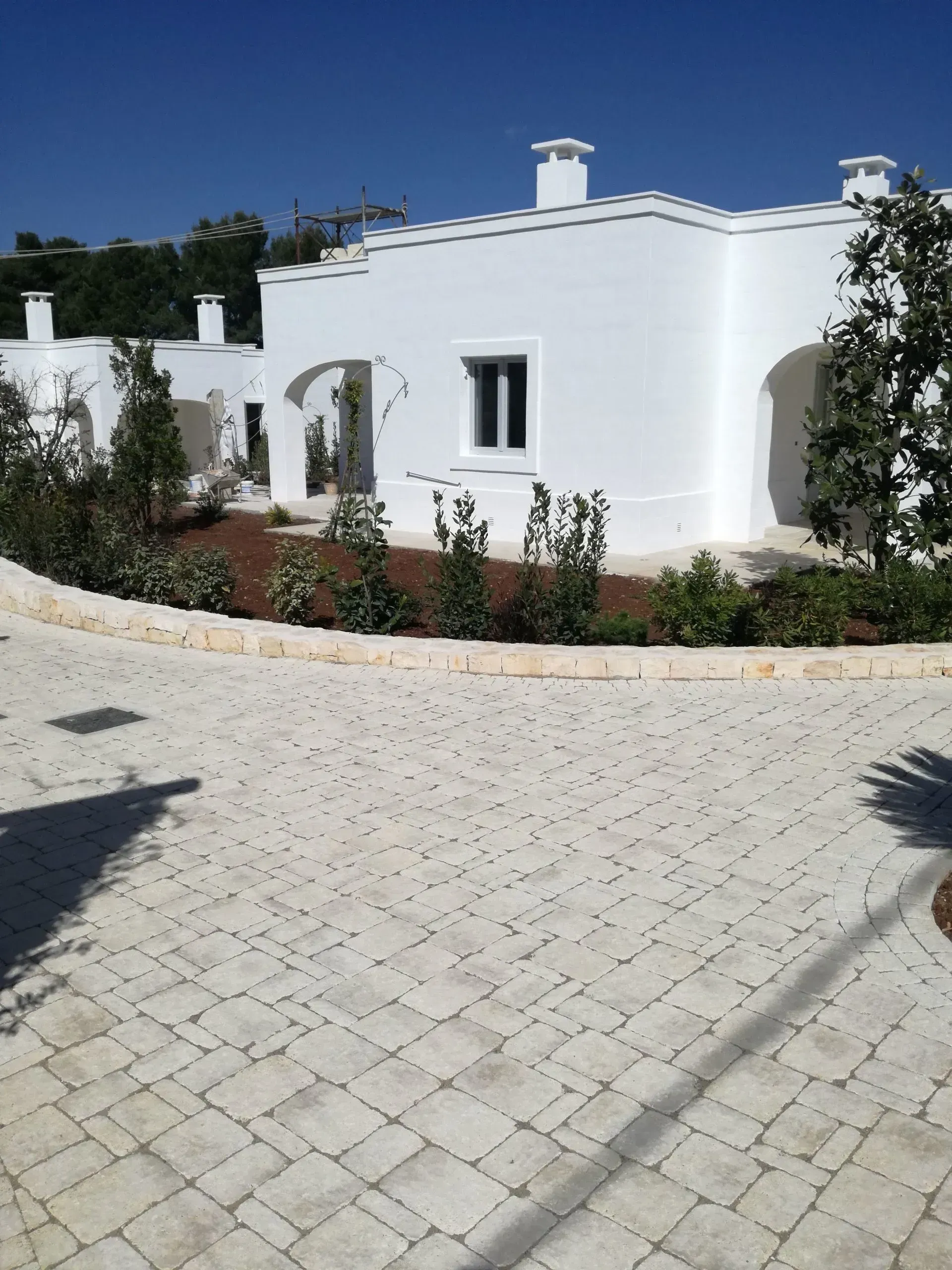 Edificio con pareti bianche, ingressi ad arco e vialetto pavimentato sotto un cielo azzurro.
