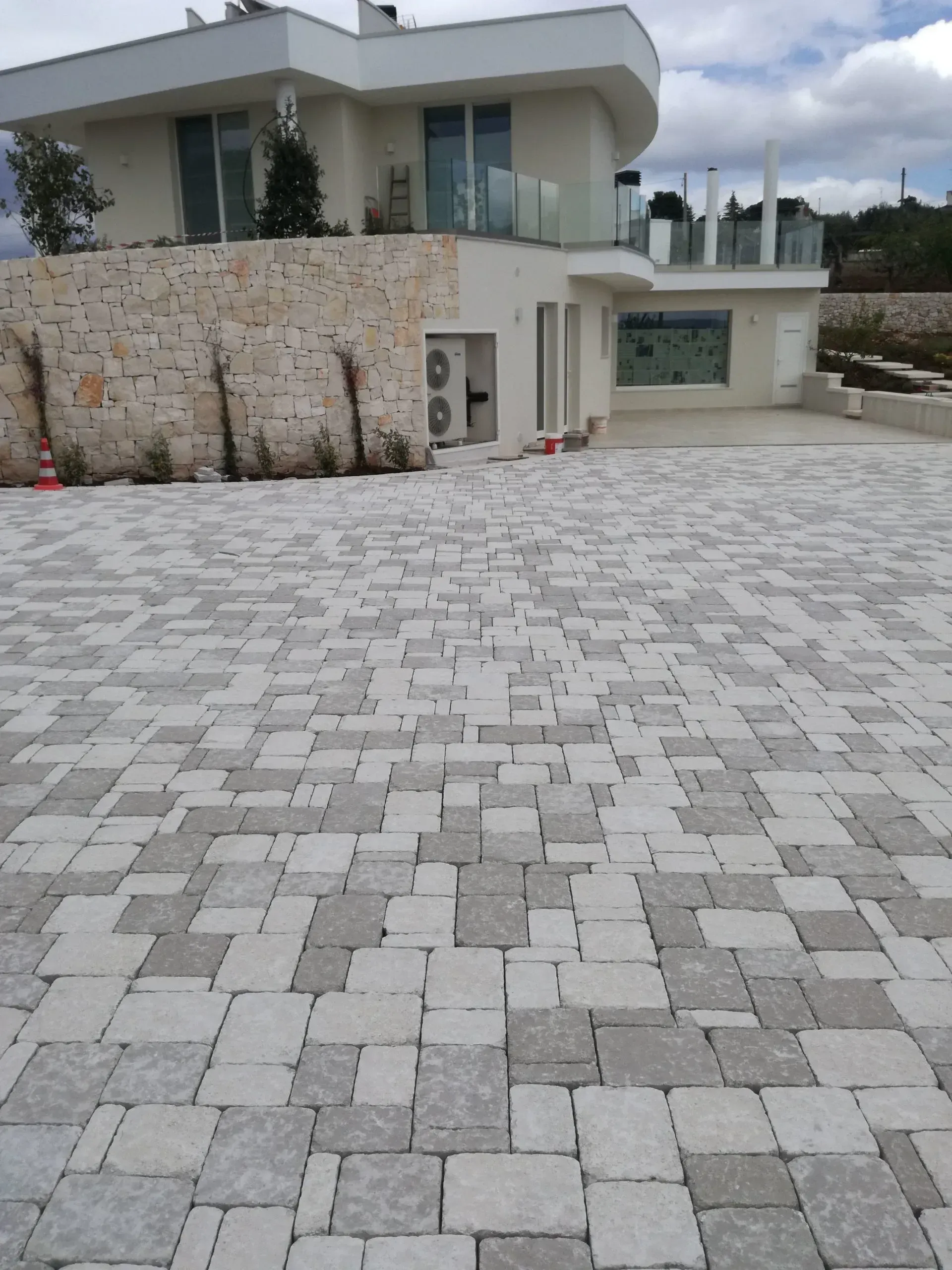 Il vialetto d'accesso pavimentato con pietre rettangolari grigio chiaro e scuro conduce a una moderna casa bianca.