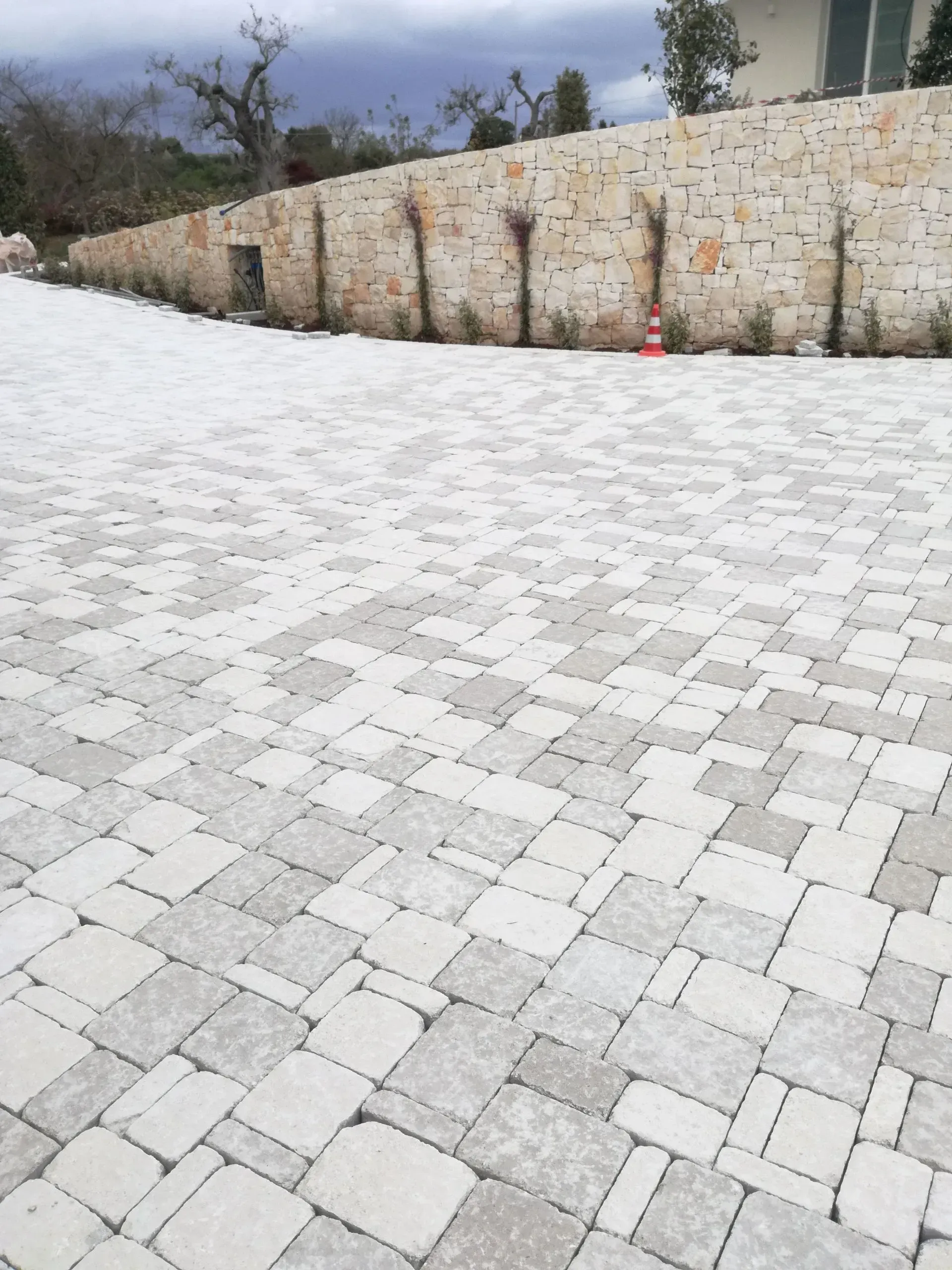 Vialetto lastricato in pietra che conduce a un muro di pietra usurato, con poca vegetazione e un cielo coperto.