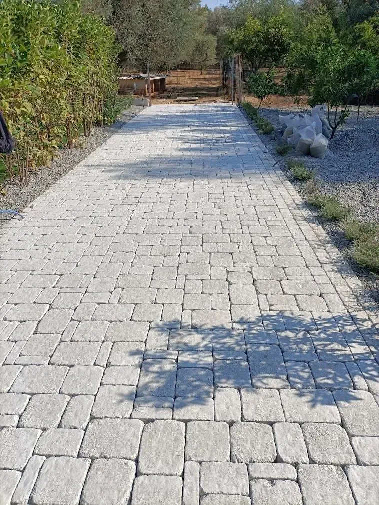 Sentiero in mattoni di pietra che conduce a un cancello di legno, circondato dal verde e illuminato dalla luce del sole.