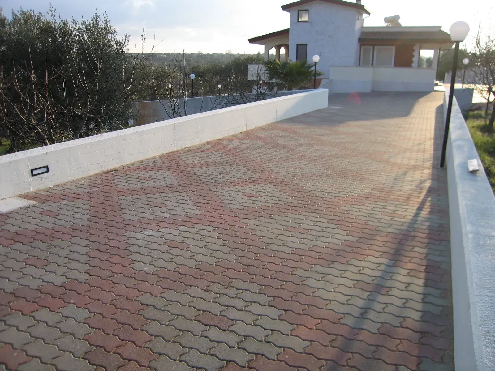 Un vialetto pavimentato con mattoni rossi e grigi ad incastro conduce a una casa bianca con una torre rotonda.