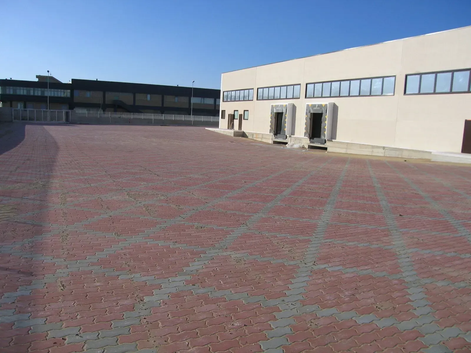Area pavimentata in mattoni rossi e grigi di fronte a un edificio beige chiaro con finestre e banchine di carico.