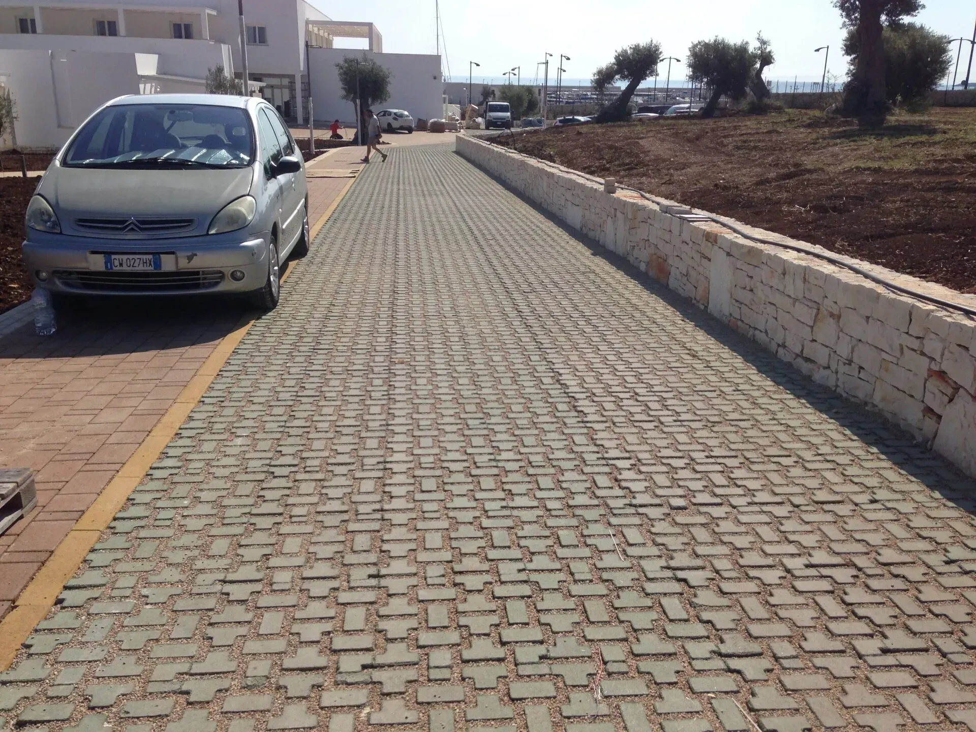 Auto parcheggiata su una strada lastricata accanto a un basso muro bianco, vicino a un edificio, in una giornata di sole.