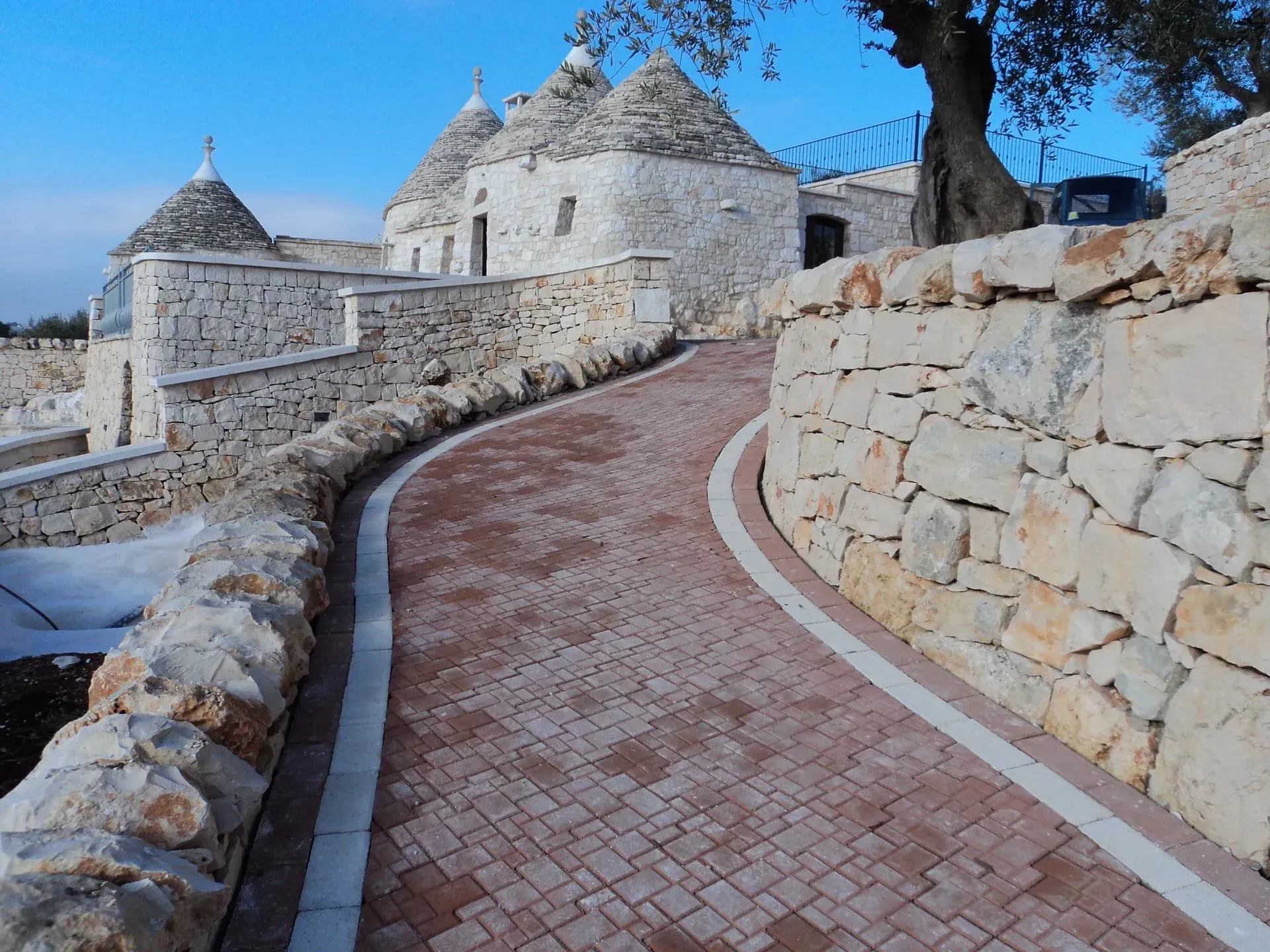 Un sentiero in pietra conduce ai tradizionali trulli bianchi con tetti conici, Puglia, Italia.