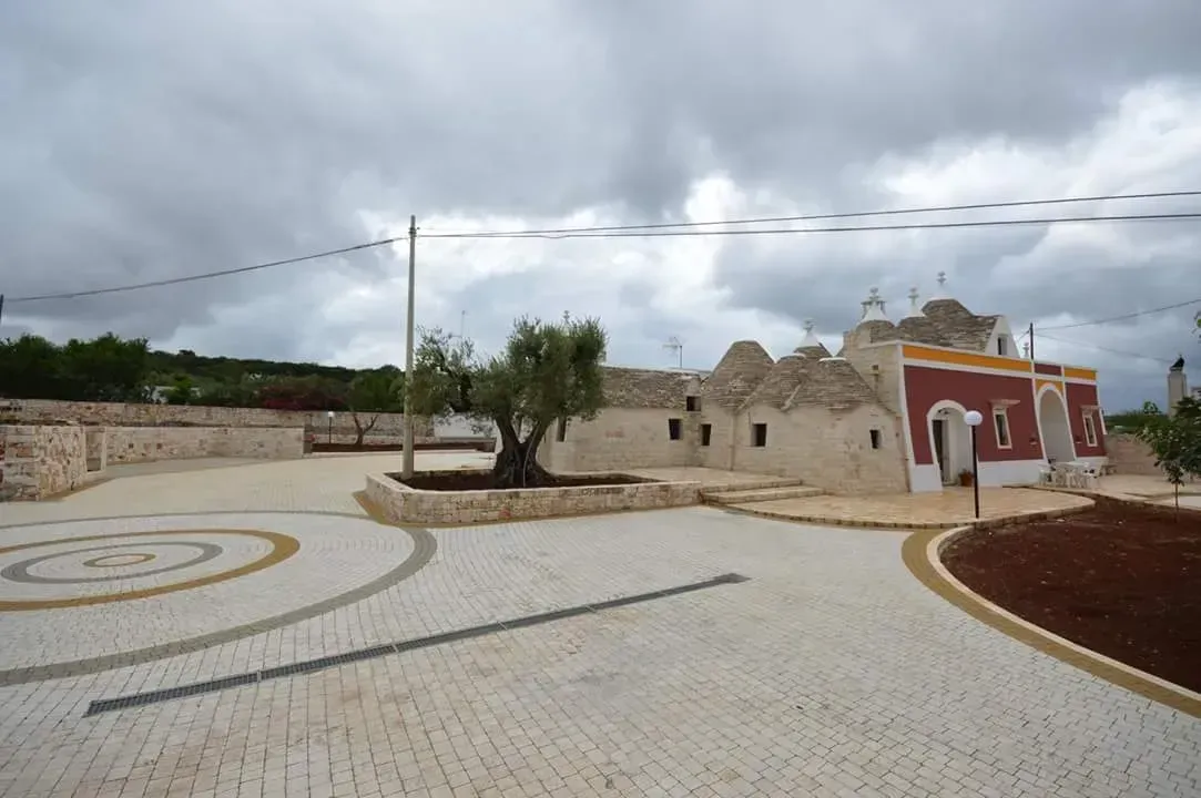 Cortile con edifici in pietra, tra cui una chiesa con la facciata rossa, sotto un cielo nuvoloso.