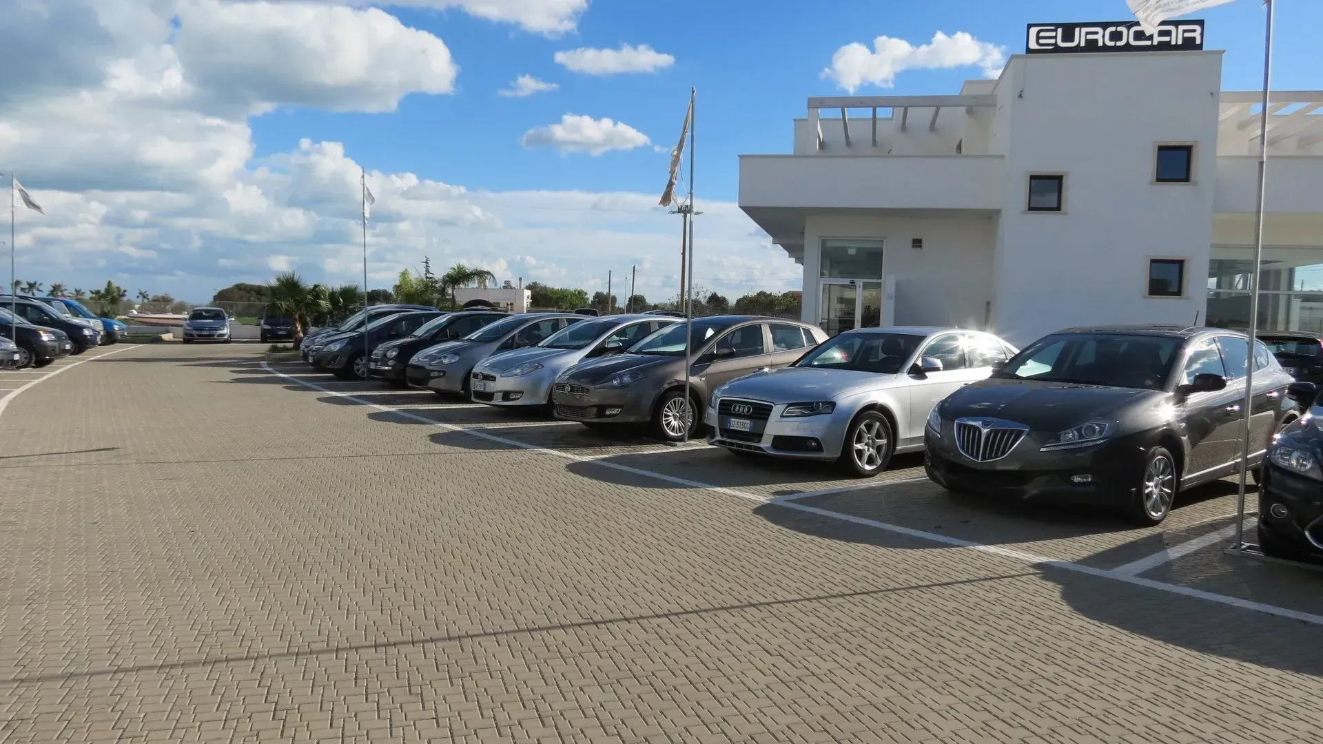 Auto parcheggiate in un parcheggio all'esterno di un edificio bianco con la scritta 