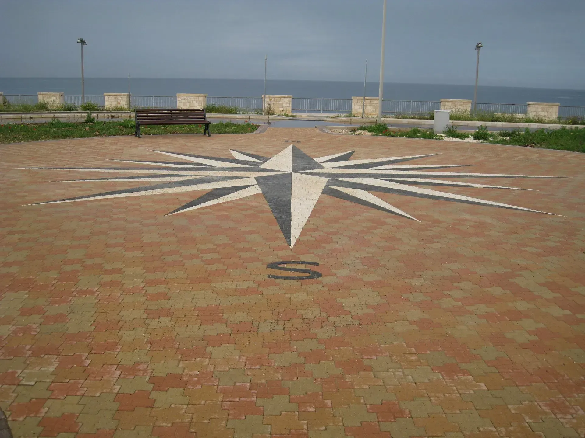 Mosaico raffigurante una rosa dei venti su un patio in mattoni con vista sul mare. Contrassegnato con la lettera 
